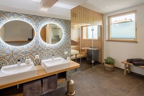 A modern bathroom with two sinks, large mirrors, patterned tiles, and a window with blinds. - Holiday apartment in Kronburg with sauna (Kronburg)