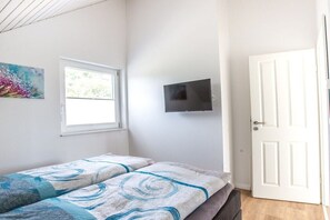 Quarto com cama, janela, porta e televisão na parede.