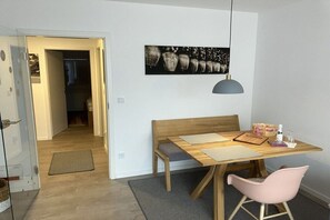 Quarto com mesa de madeira, um banco, uma cadeira rosa, luminária pendente e quadro na parede.