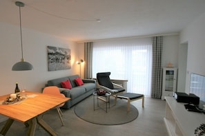 Uma sala de estar moderna com um sofá, poltrona, mesa de jantar e um quadro na parede.