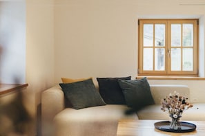 A living room with a sofa, pillows, a small table, and a window. - high-quality with sauna (Ruhpolding)