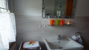 Un baño con lavamanos blanco, un espejo y repisas con tazas y una toalla.