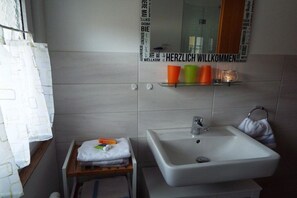 Ein Badezimmer mit einem weißen Waschbecken, einem Spiegel und einem Regal mit Tassen und einem Handtuch.