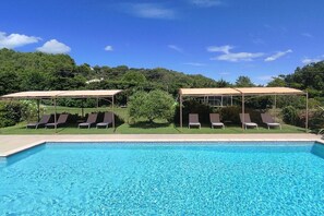 Piscina com espreguiçadeiras e áreas com sombra.