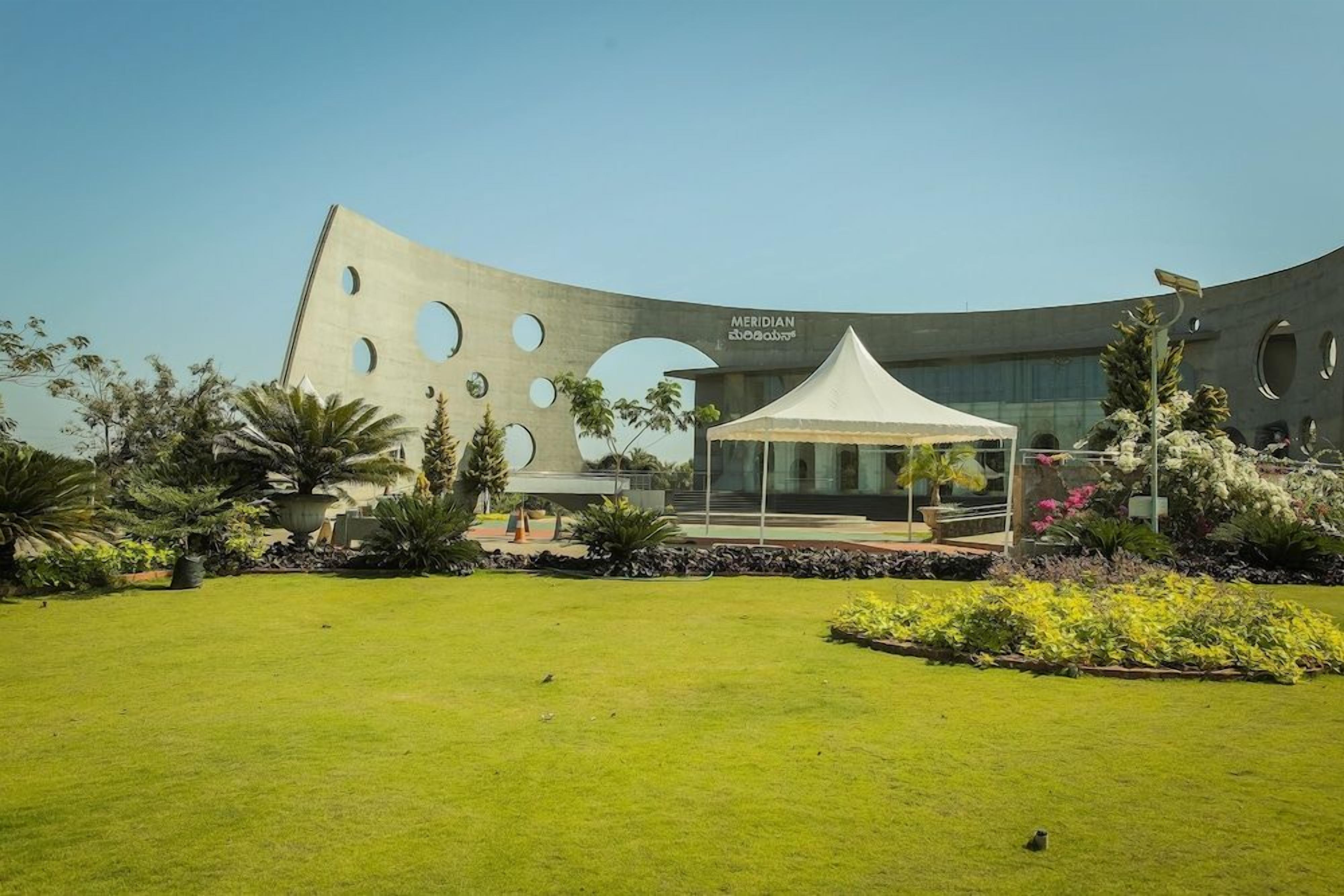 A modern building with a unique curved facade and circular cutouts, a white tent, and well-maintained landscaping.