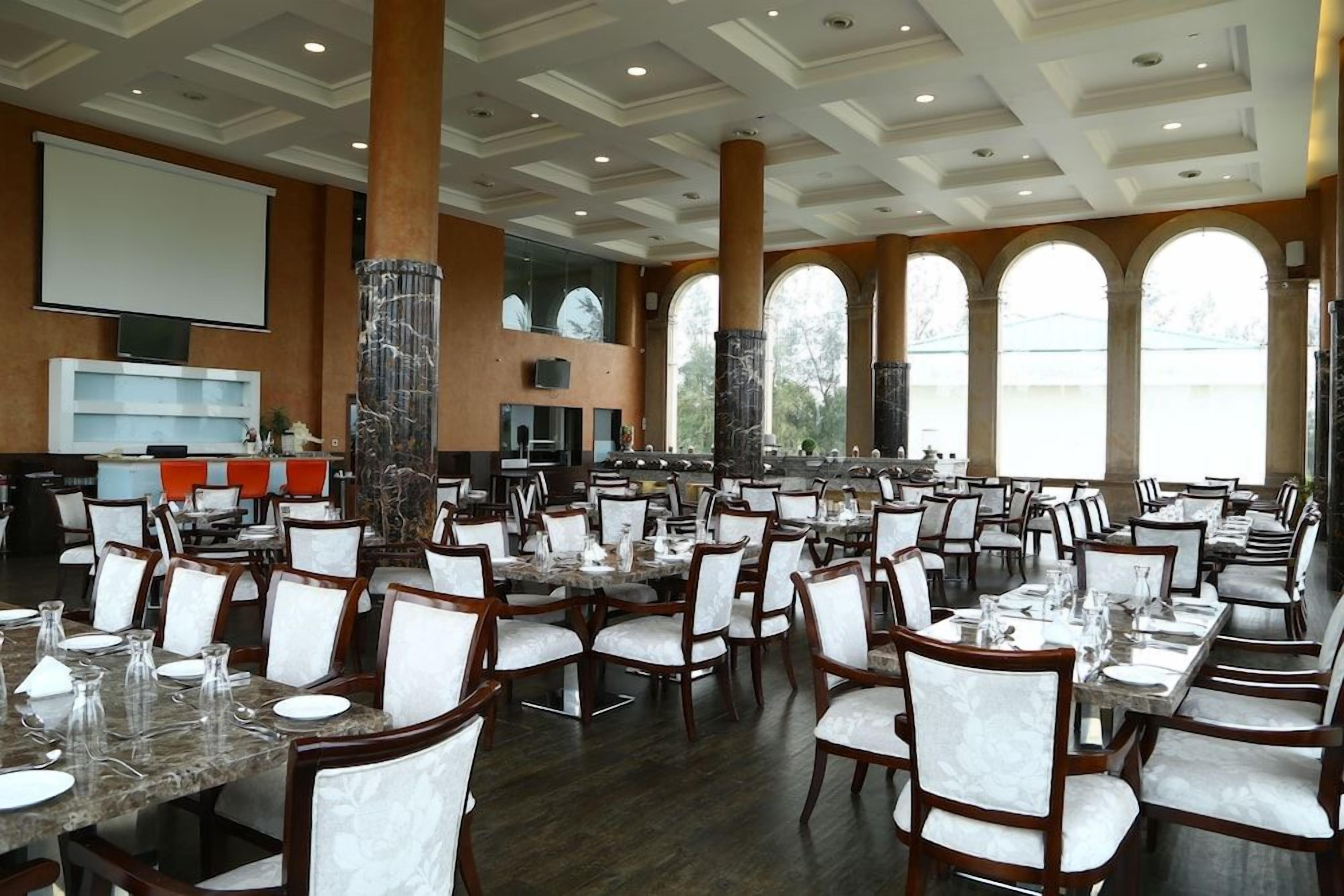 A large dining area with multiple tables and chairs, a screen, and a pillar with a decorative base.
