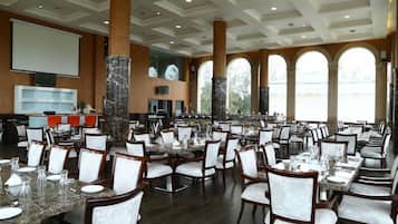 A large dining area with multiple tables and chairs, a screen, and a pillar with a decorative base.