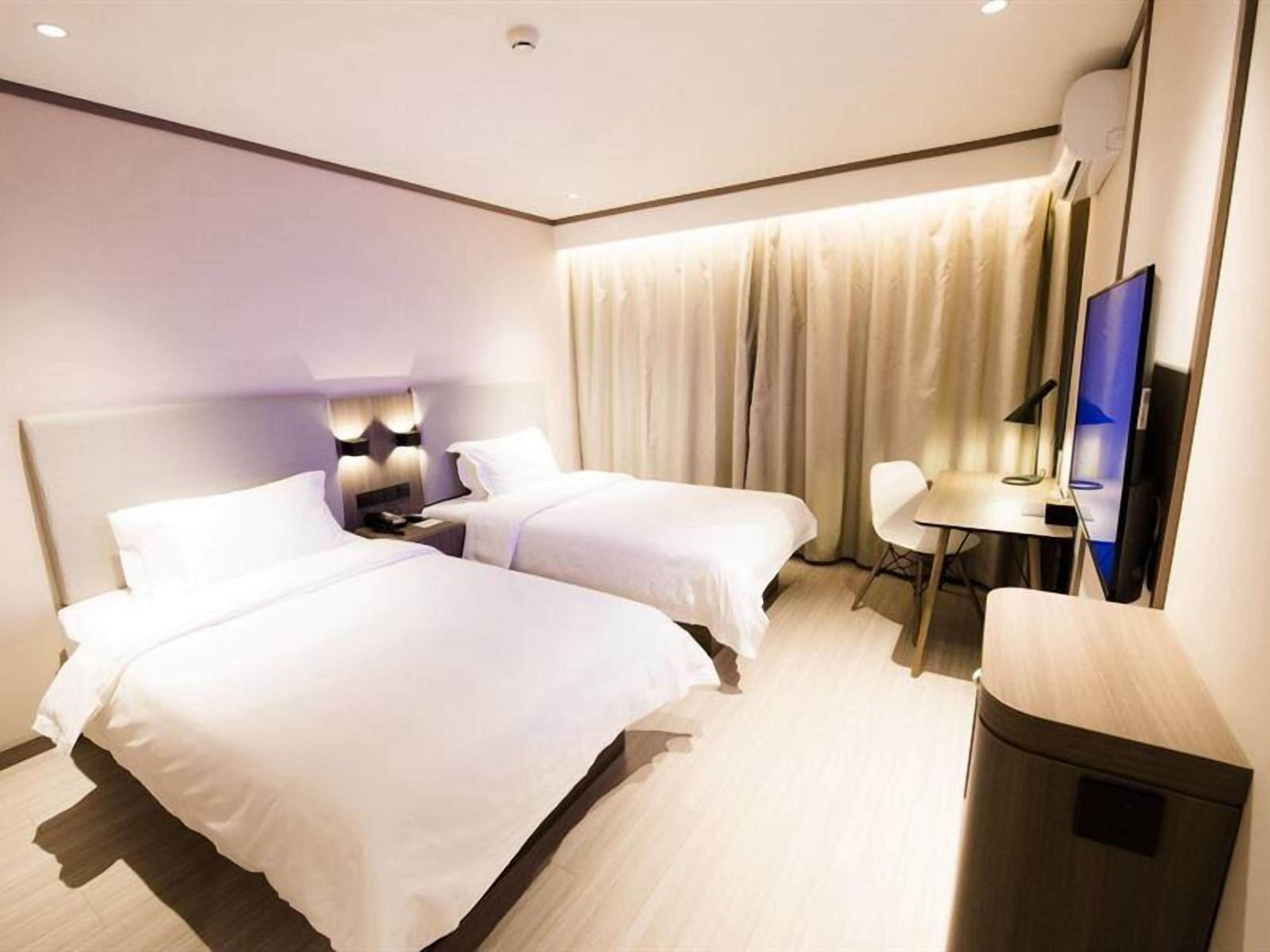 Habitación de hotel con dos camas, un escritorio, una silla, un televisor y un cesto de basura.