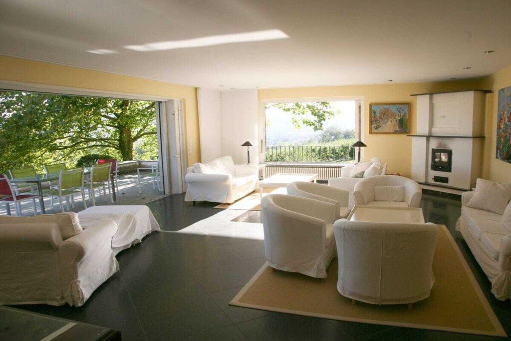 A modern living room with white furniture, a fireplace, and a view of greenery outside.