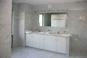 A modern bathroom with a marble wall, a large mirror, a double sink vanity, and a shower area. - "Stutengarten Estate" (Öhningen)