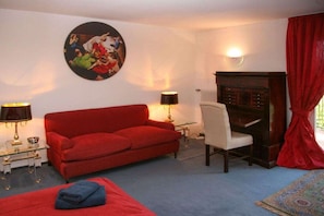 A room with a red sofa, a white chair, a small table, a lamp, a radiator, and a red curtain. - "Stutengarten Estate" (Öhningen)