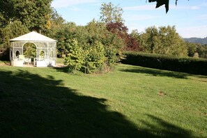 A gazebo with a lattice roof and a small table, surrounded by a well-maintained lawn and trees.