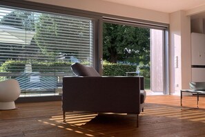 Ein modernes Wohnzimmer mit einer Couch, einem runden Tisch und einem großen Fenster mit Jalousien.