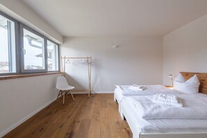 Ein Hotelzimmer mit großem Fenster, Holzboden, Bett mit weißer Bettwäsche und einem Holz-Kopfstück.