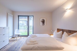 A bedroom with a large bed, a white dresser, a chair, and a view through a glass door. - Seebruck on Lake Chiemsee (Seebruck)