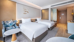 A hotel room with two beds, a desk, a chair, and a small table.