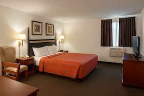Ett hotellrum med en säng, sängbord, en stol, ett skrivbord, en tv och ett fönster med gardiner.