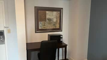 Een kleine kantoorruimte met een bureau, een stoel, een magnetron en een kunstwerk in een lijst aan de muur.