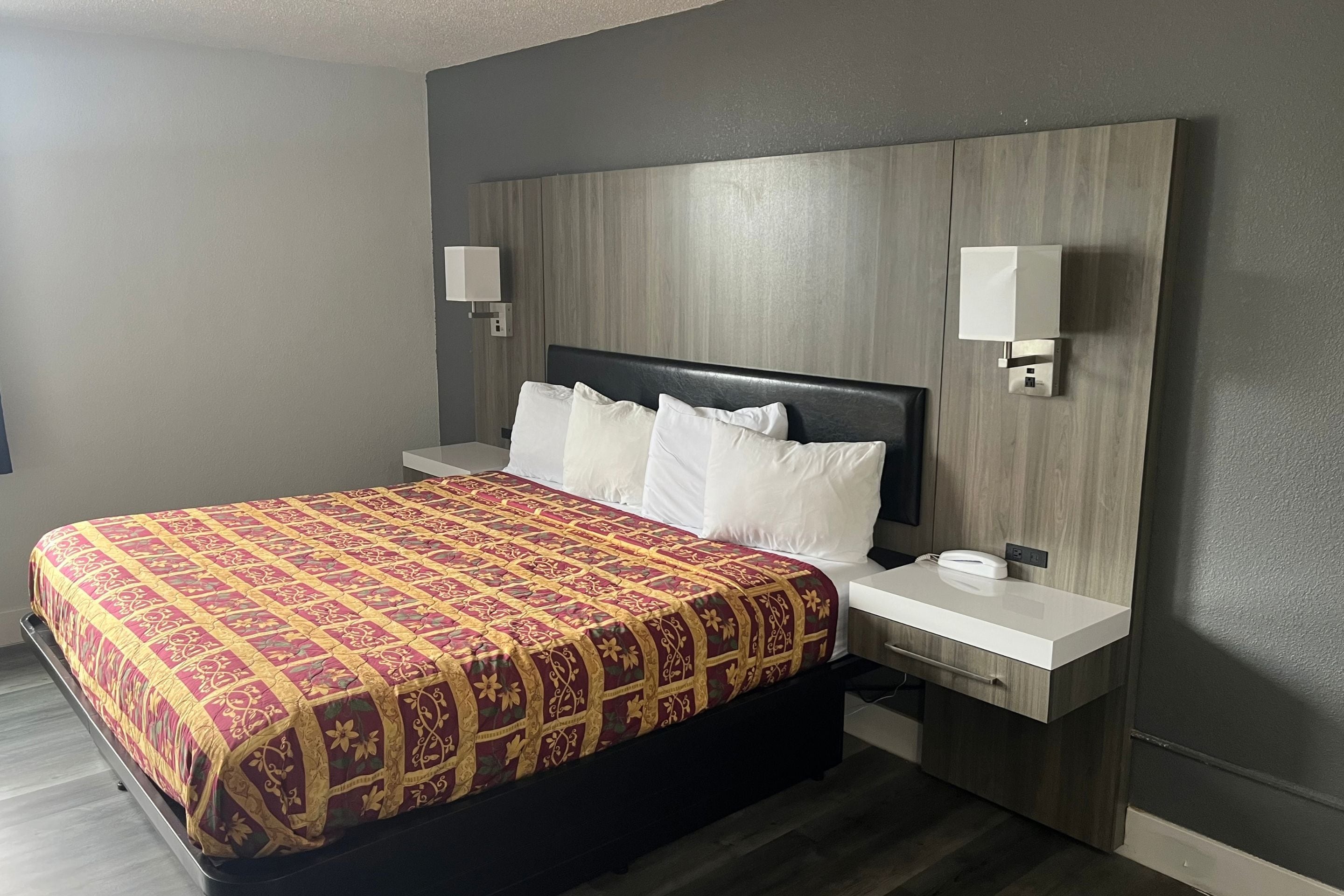 Una habitación de hotel con cama, mesitas de noche y lámparas de pared.
