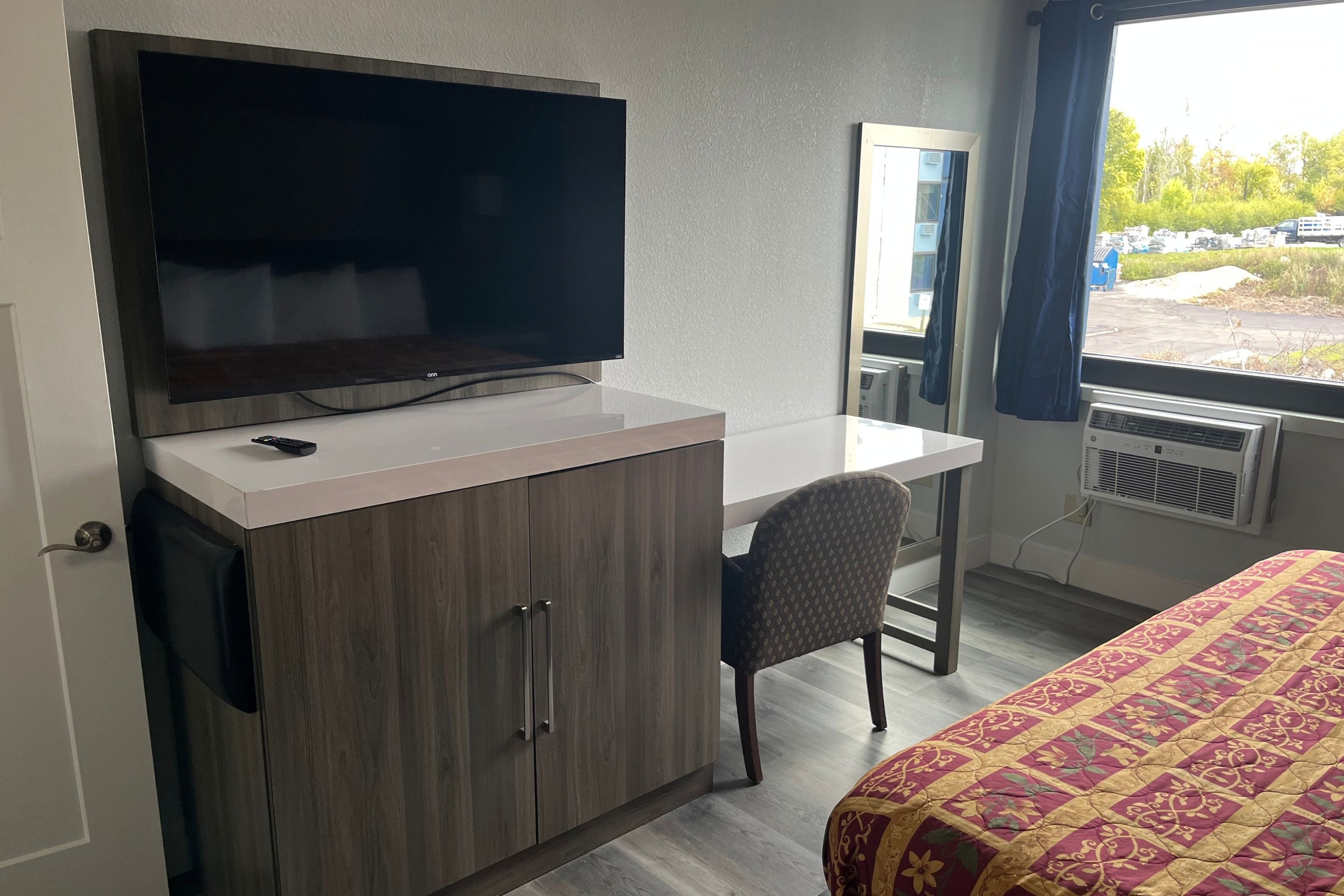 Een hotelkamer met een bed, een bureau, een televisie en een raam met uitzicht op buiten.