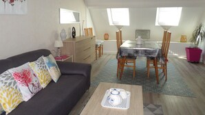 A living room with a sofa, a dining table with chairs, a coffee table, and a kitchen area with cabinets and a countertop. - Dinard-ville location 2 chambres, plage de l'écluse-commerces-transports à pieds (Dinard)
