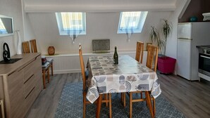 A modern kitchen with a dining area, featuring a table with a patterned tablecloth, wooden chairs, and a bottle of wine. - Dinard-ville location 2 chambres, plage de l'écluse-commerces-transports à pieds (Dinard)