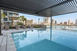 A rooftop infinity pool with a cityscape view, lounge chairs, and a covered area with a view of the marina. - StayShort - Stunning Beachfront 3-Bedroom Apartment Sleeps 5 with Infinity Pool, Skyline Views & Private Beach Access (Emaar Beach Front)