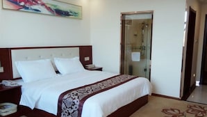 Une chambre d’hôtel avec un grand lit, une table de chevet, une commode, une douche en verre et un sol recouvert de moquette.
