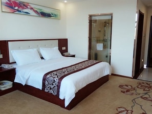 Habitación de hotel con una cama grande, una mesita de noche, una lámpara y una ducha con mampara, además de piso alfombrado.