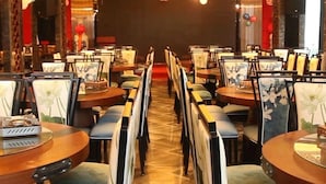 Une salle à manger avec des rangées de tables et de chaises, une scène à l’avant et des ballons.