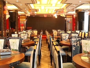 Un comedor con filas de mesas y sillas, un escenario al frente y globos.