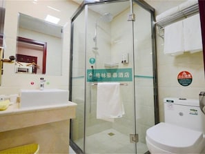 Un baño de hotel con ducha de mampara de vidrio, un lavamanos y un inodoro.