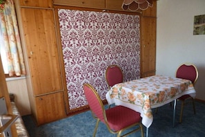 Ein Zimmer mit einem Tisch, zwei Stühlen, einem gemusterten Vorhang und Holzwänden.