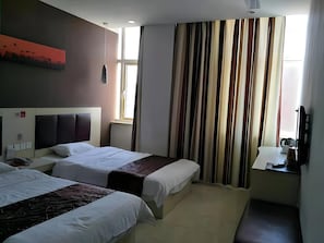 Quarto de hotel com duas camas, uma janela com cortinas, mesa de cabeceira com abajur e televisão fixada na parede.