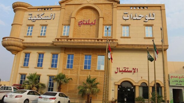A building with multiple signs in Arabic, including 'Al-Sabah Hotel' and 'Al-Sabah Hotel'. There are flags, palm trees, and parked cars in front. - Lailaty Hotel Apart (Riyadh)
