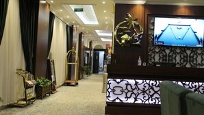 A hotel lobby with a reception desk, a television screen displaying a pool table, and a corridor leading to other areas. - Lailaty Hotel Apart (Riyadh)