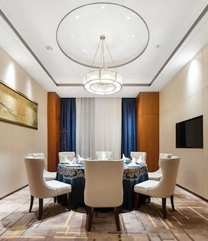 A hotel room with a round dining table, four chairs, a chandelier, a painting on the wall, and a television mounted on the wall. - Metropolo Wuhan Optics Valley Convention&exhibition Center Hotel (Wuhan)