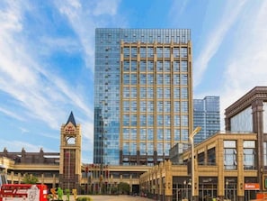 A modern building with a glass facade, a prominent tower with a pointed top, and a series of smaller buildings with a mix of architectural styles. - Metropolo Wuhan Optics Valley Convention&exhibition Center Hotel (Wuhan)