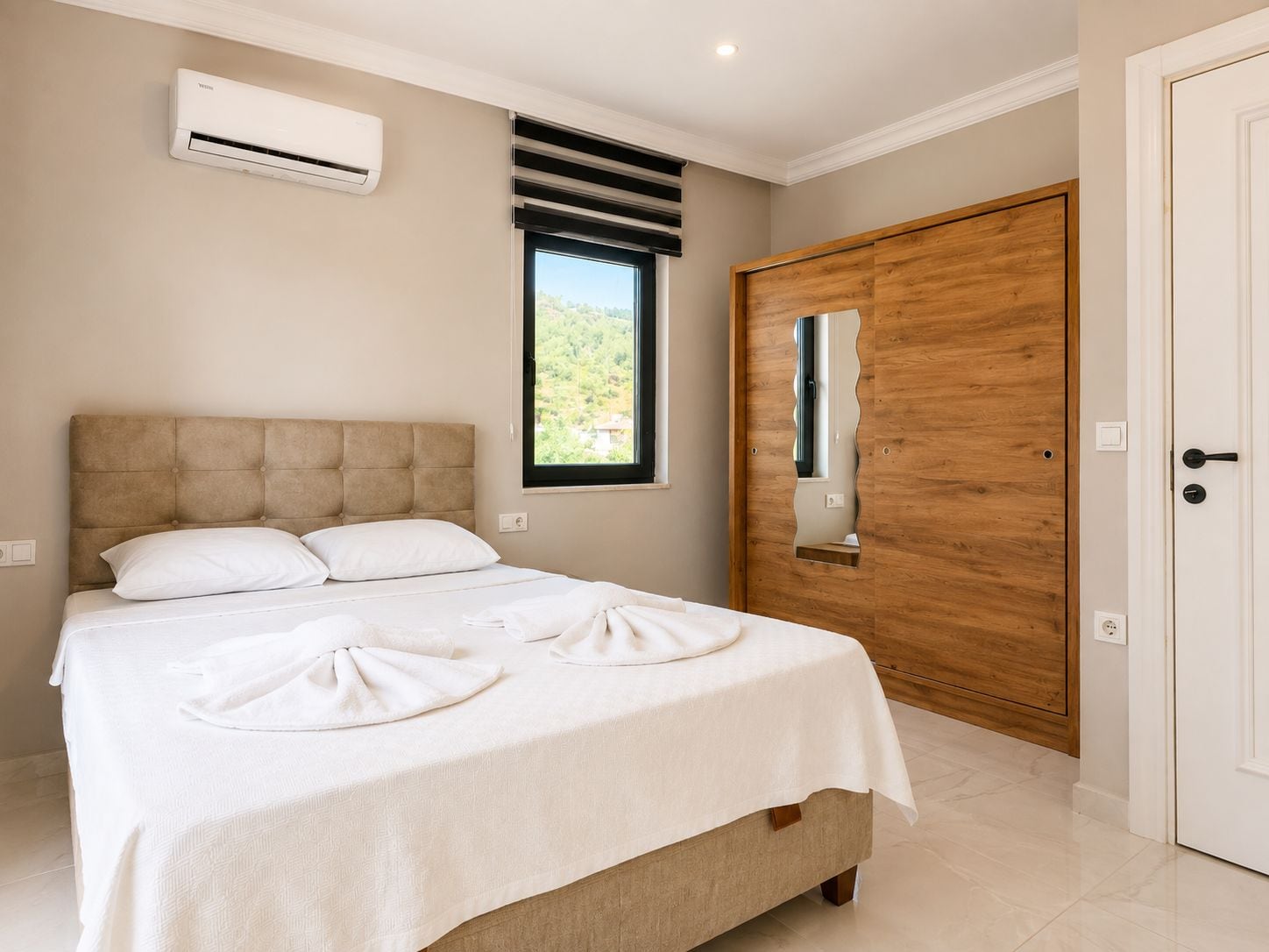 Une chambre à coucher avec un lit, un appareil de climatisation, une fenêtre donnant sur un beau paysage et une porte en bois.