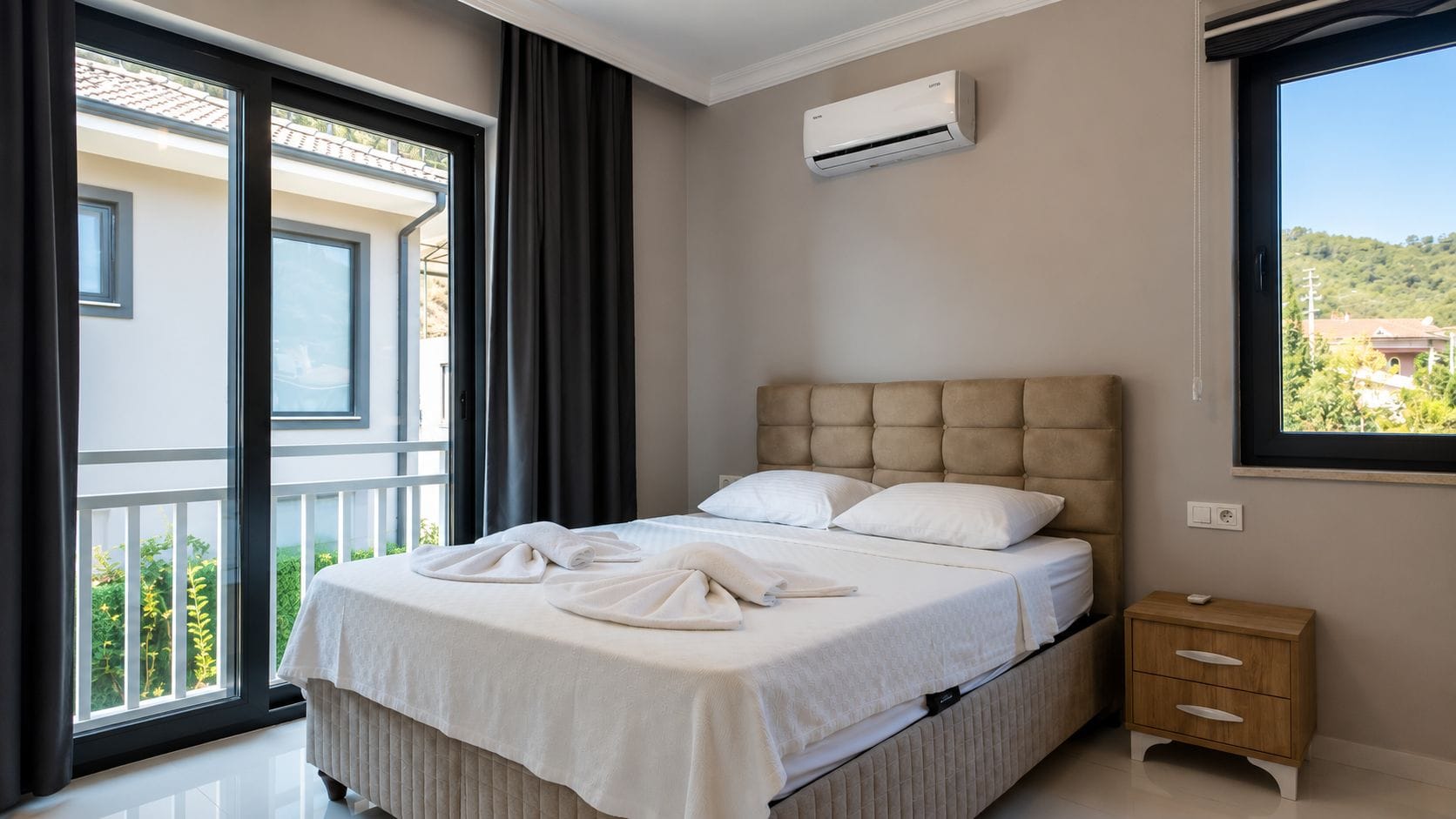 Ein Hotelzimmer mit Bett, Nachttisch, Klimaanlage und Fenster mit Blick nach draußen.