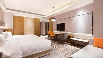 A modern hotel room with a large bed, a desk, a sofa, and a TV.