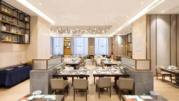 A spacious restaurant with multiple dining tables and chairs, a bar area with shelves, and a modern ceiling design.