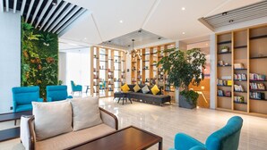 A modern lobby with a sofa, chairs, a coffee table, and a large bookshelf. - Rezen Select Hangzhou Xiaoshan Airport (Hangzhou)