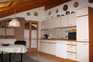 Cozinha com armários brancos, lava-louças e fogão. Há uma mesa de jantar com cadeiras.
