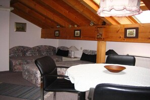 Um quarto aconchegante com teto de madeira, um conjunto de sofás, uma mesa de jantar com uma tigela e quadros nas paredes.