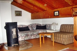 Uma sala de estar com sofá, um estofado estampado, mesa e lareira a lenha.