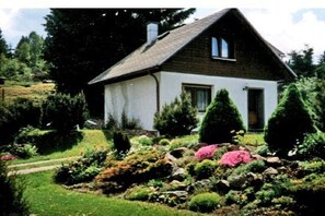 A single-story house with a gabled roof, surrounded by a well-maintained garden with various plants and shrubs. - Holiday home in Stützerbach with Wi-Fi (Stützerbach)