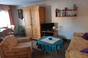 A living room with a wooden cabinet, a television, a round table with a blue tablecloth, and a bookshelf. - Holiday home in Stützerbach with Wi-Fi (Stützerbach)