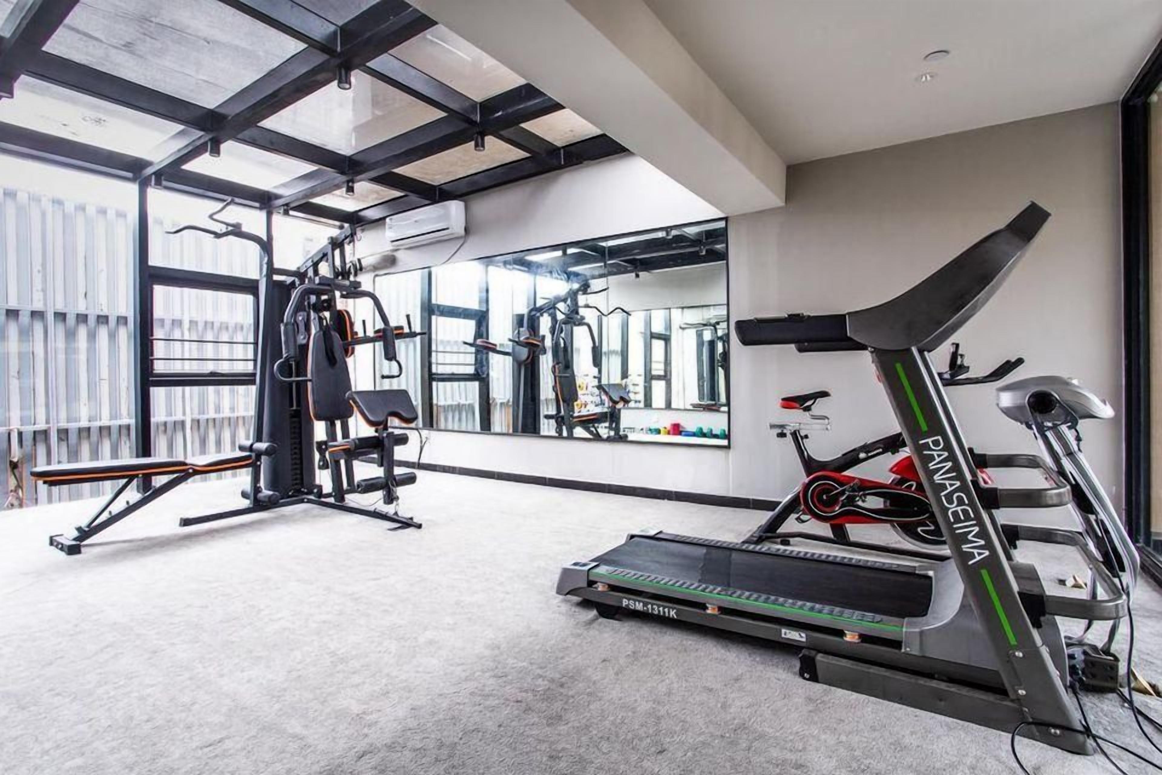 A gym with exercise equipment including a treadmill, weight machines, and a mirrored wall.