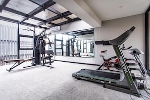 A gym with exercise equipment including a treadmill, weight machines, and a mirrored wall. - Yuhuayuan Design Hotel (Haikou)